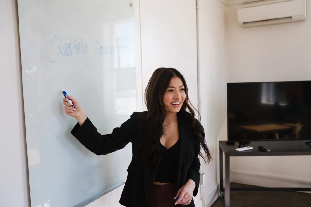 Young lady teacher pointing at white board with marker